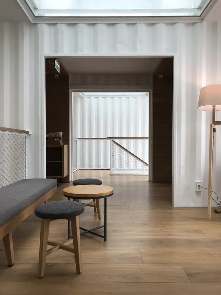 Interno con pareti in lamiera dei container dipinte di bianco, pavimento in legno e lucernario, Starbucks Hualienbay Store