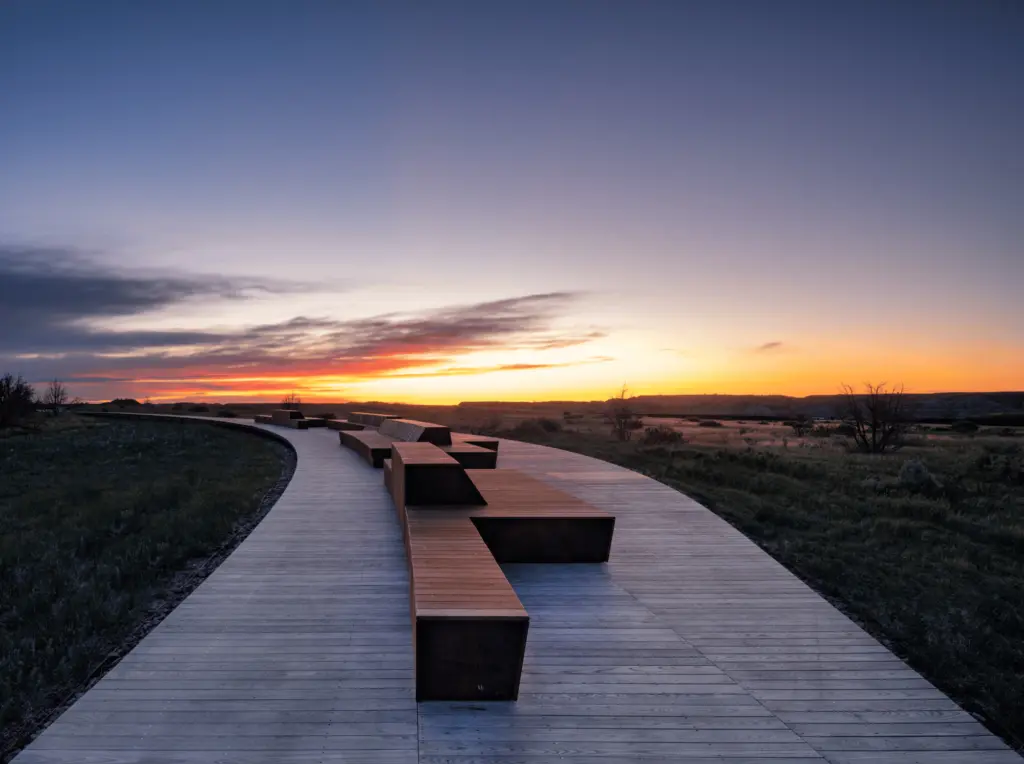 Sedute in acciaio corten lungo la passerella al tramonto sulla prateria