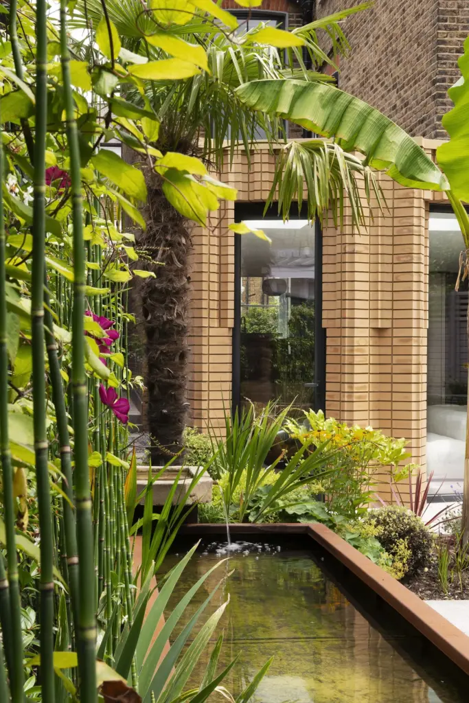 Giardino subtropicale di W House visto tra le foglie, con l'estensione in mattoni sullo sfondo